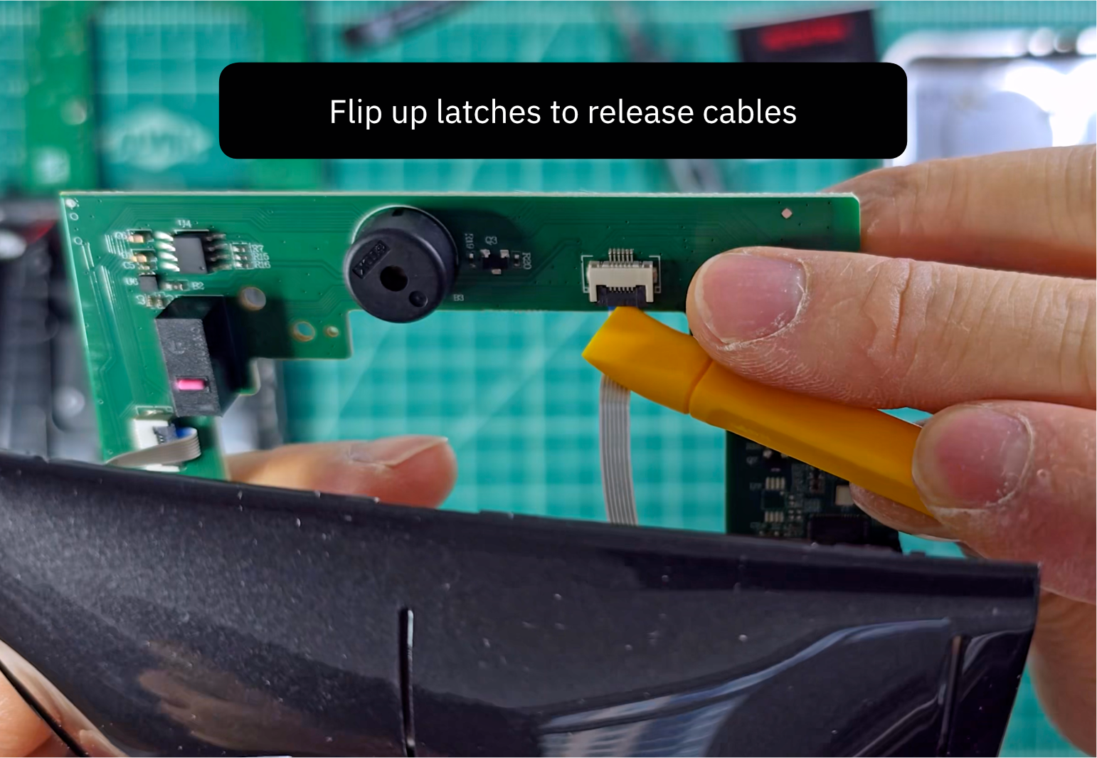 Flipping up a black FFC latch with a pry tool to release a ribbon cable from the back of the board